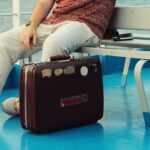 A man sits on a ferry with a vintage leather suitcase on a sunny day.